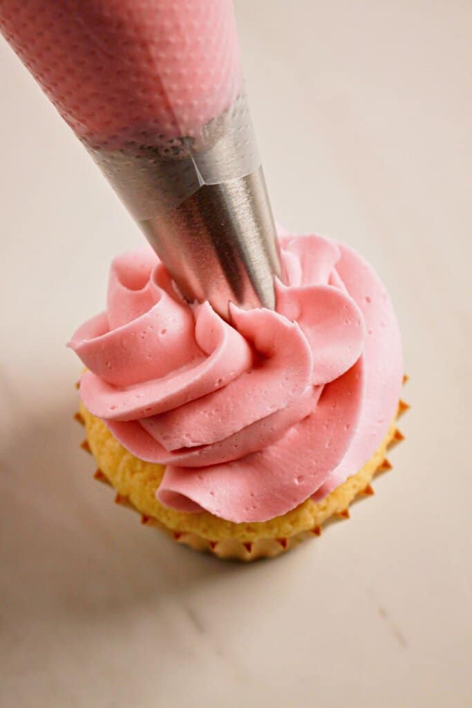 Frosting being piped on top of a cupcake.