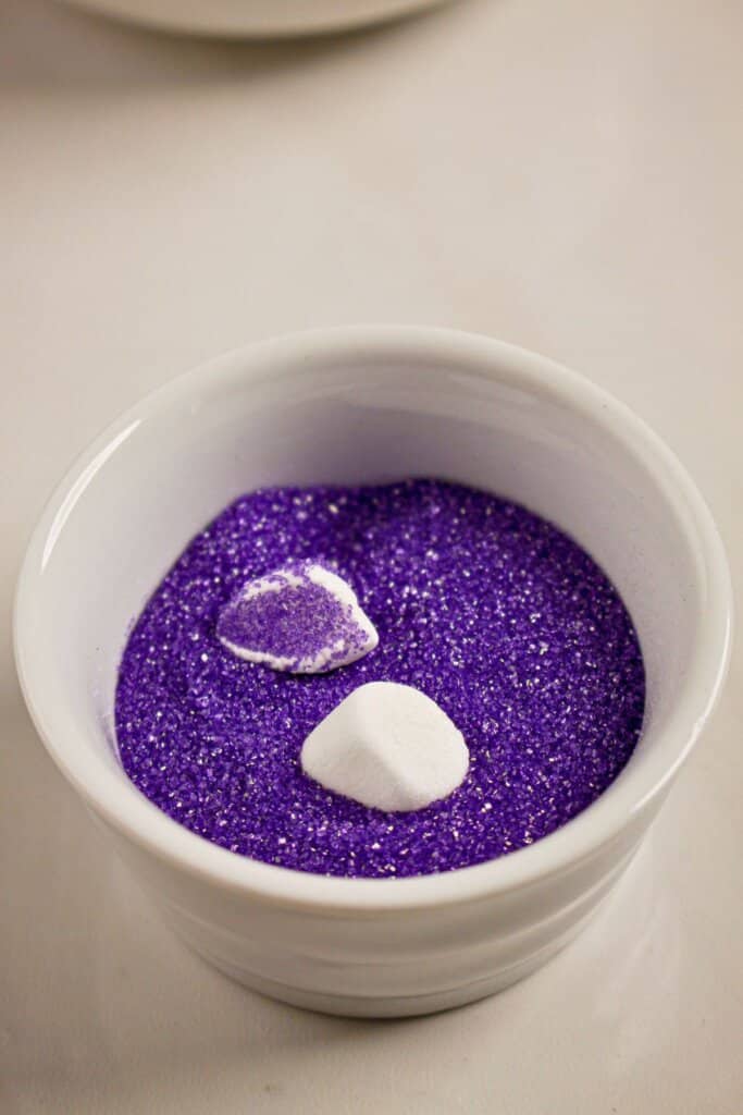 Cut marshmallow being dipped in colored sugar.
