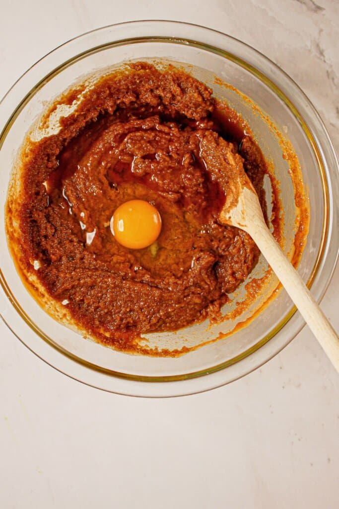 Egg being mixed into dough in a glass bowl.