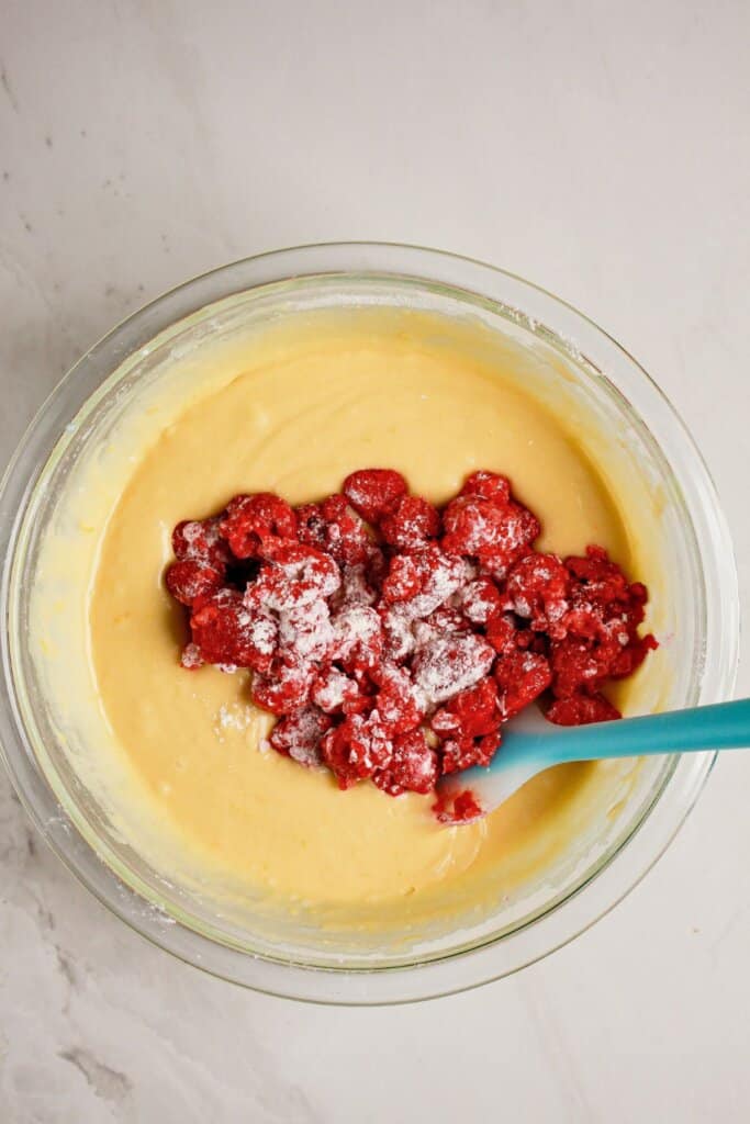 Raspberries being folded into batter in a glass mixing bowl.