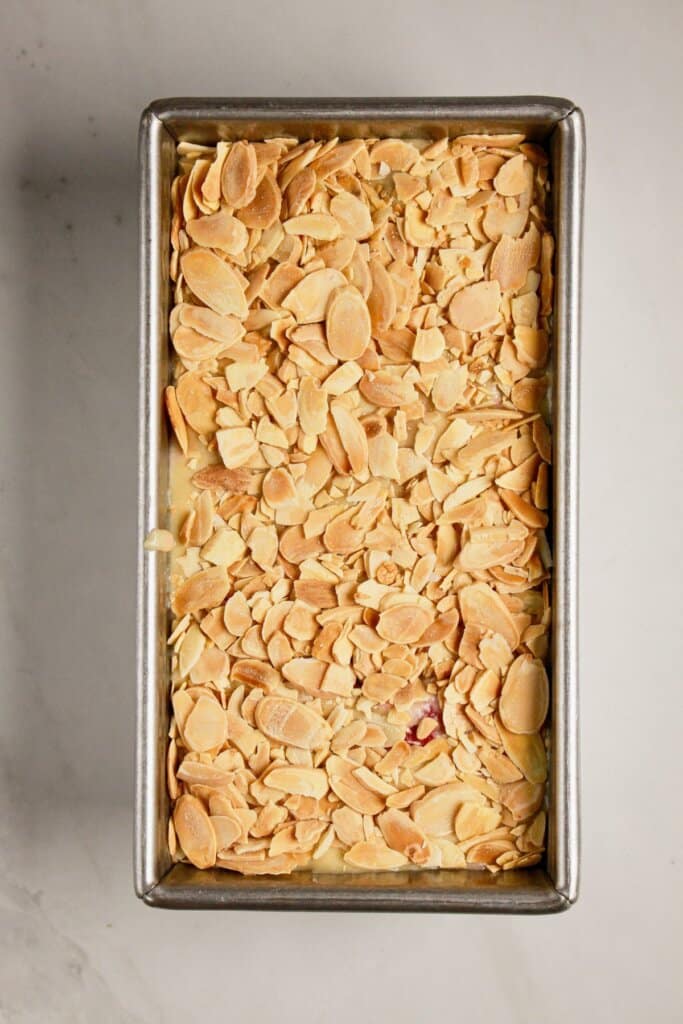 Sliced almonds on top of batter in a loaf pan.