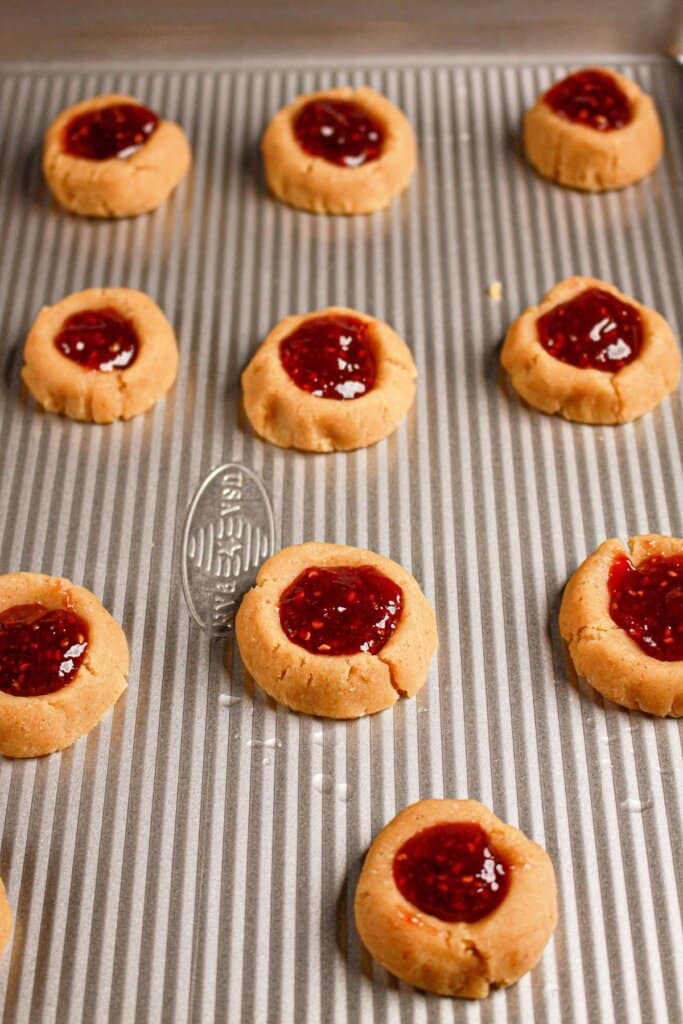Jam being added to dough balls on a baking sheet.