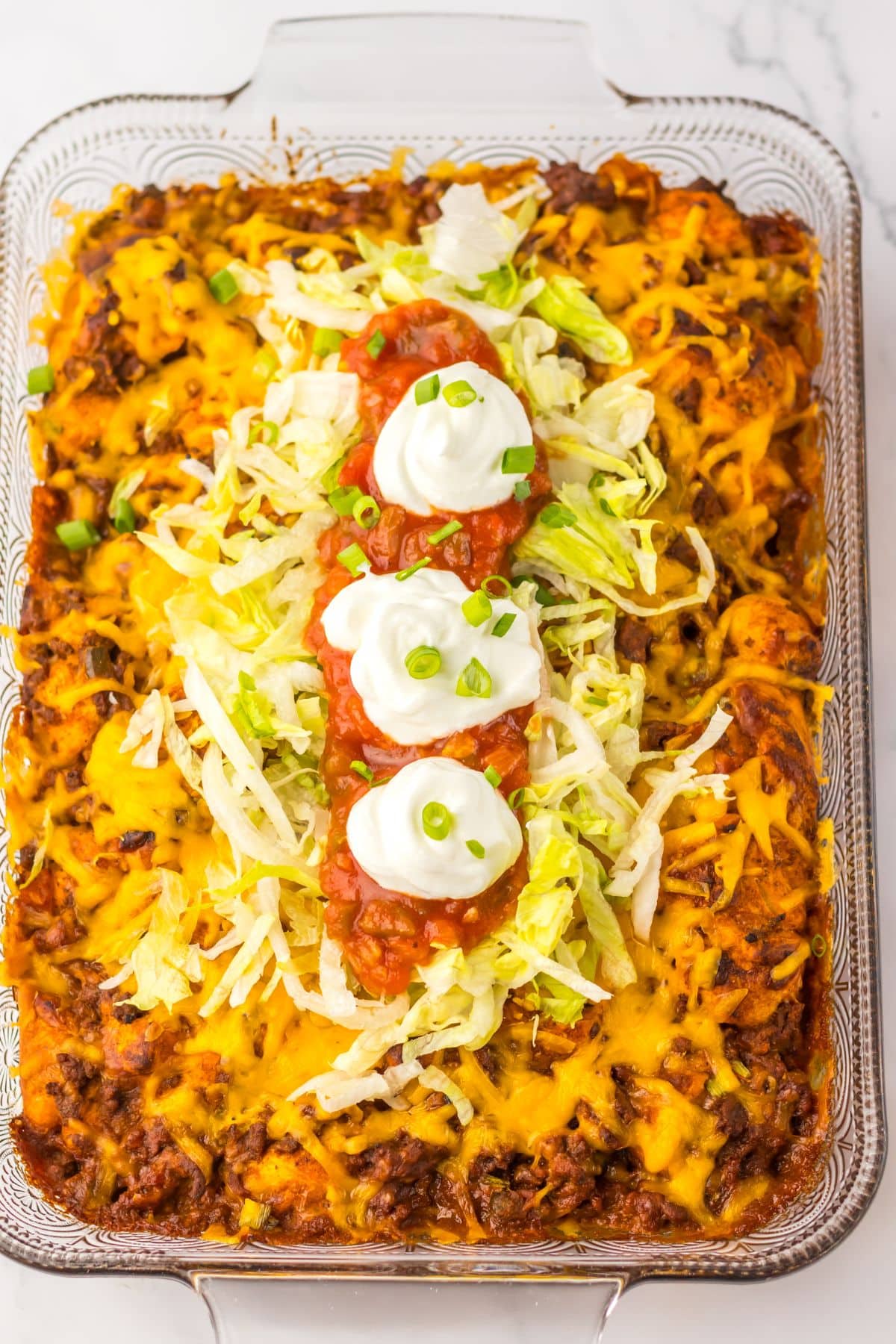 Taco bubble up bake in a glass baking dish topped with salsa, lettuce, and sour cream.