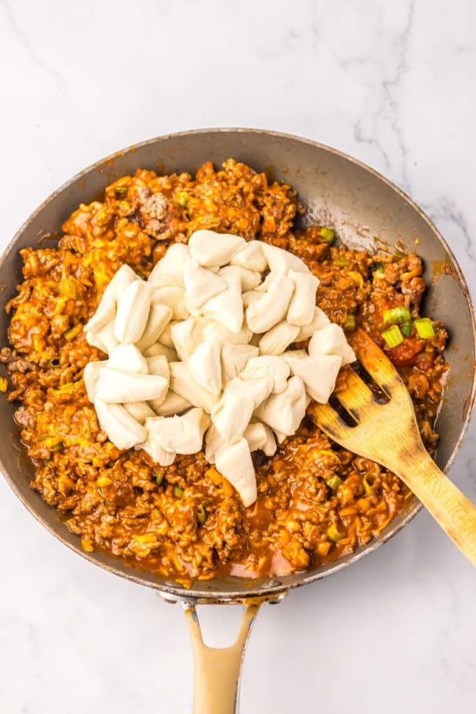 Dough pieces being stirred into ground beef in a large skillet.