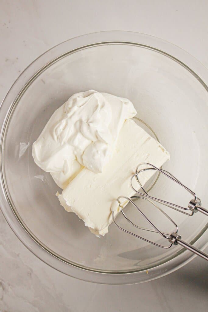 Sour cream and cream cheese being mixed in a glass bowl.