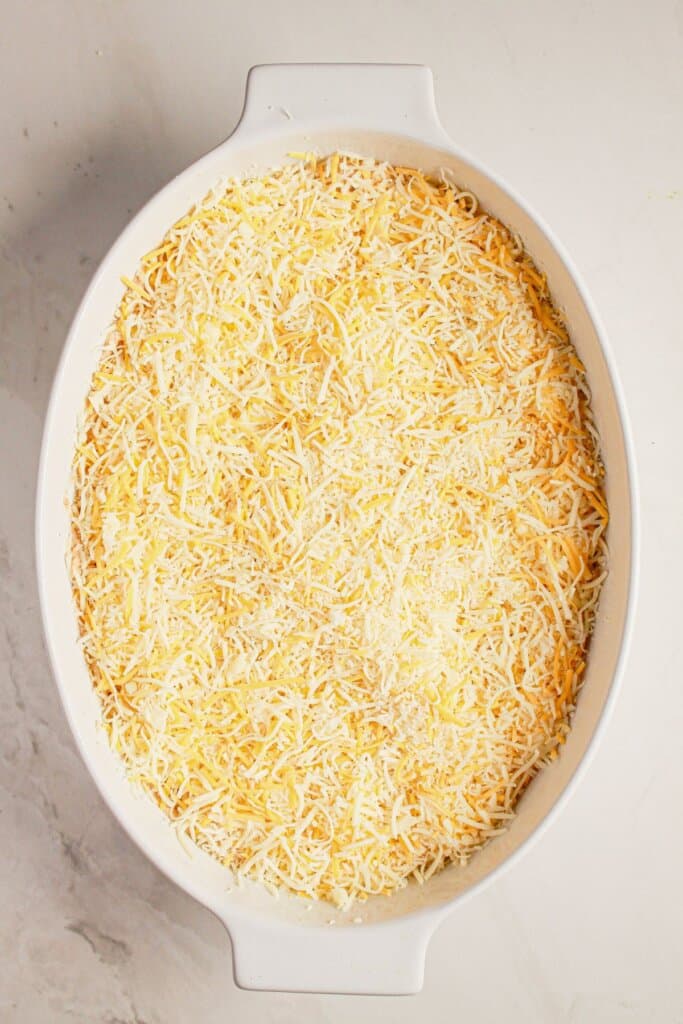 Shredded cheese being sprinkled on top, in a casserole dish.