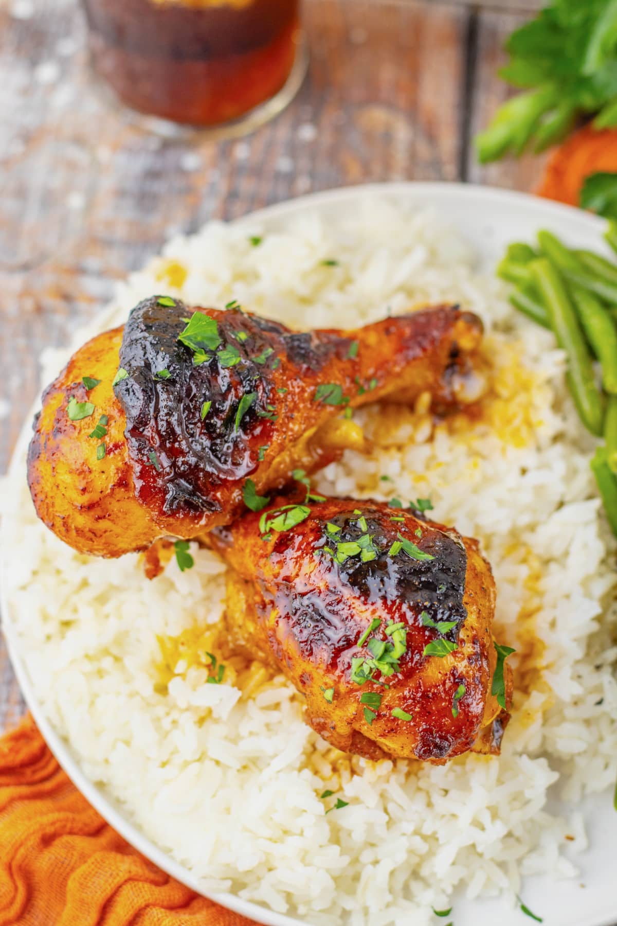 Two cajun chicken legs on a white plate with rice and green beans.