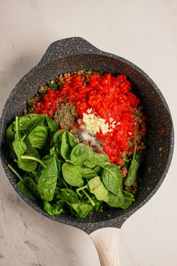 Spinach and diced tomatoes being added to a large skillet.