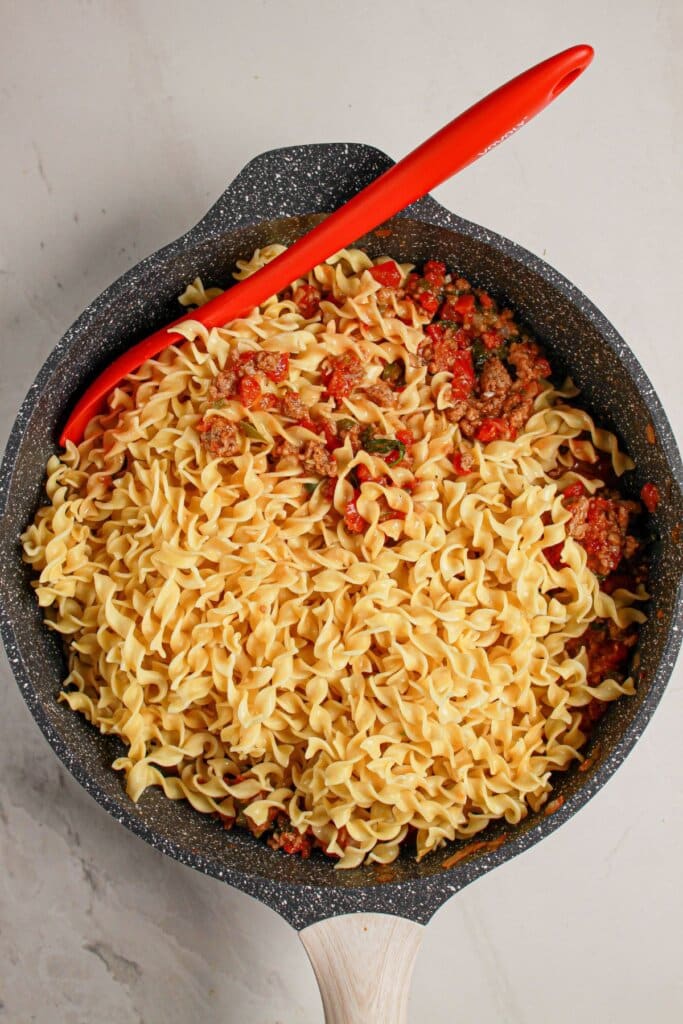 Egg noodles being stirred into a meat and veggie mixture.