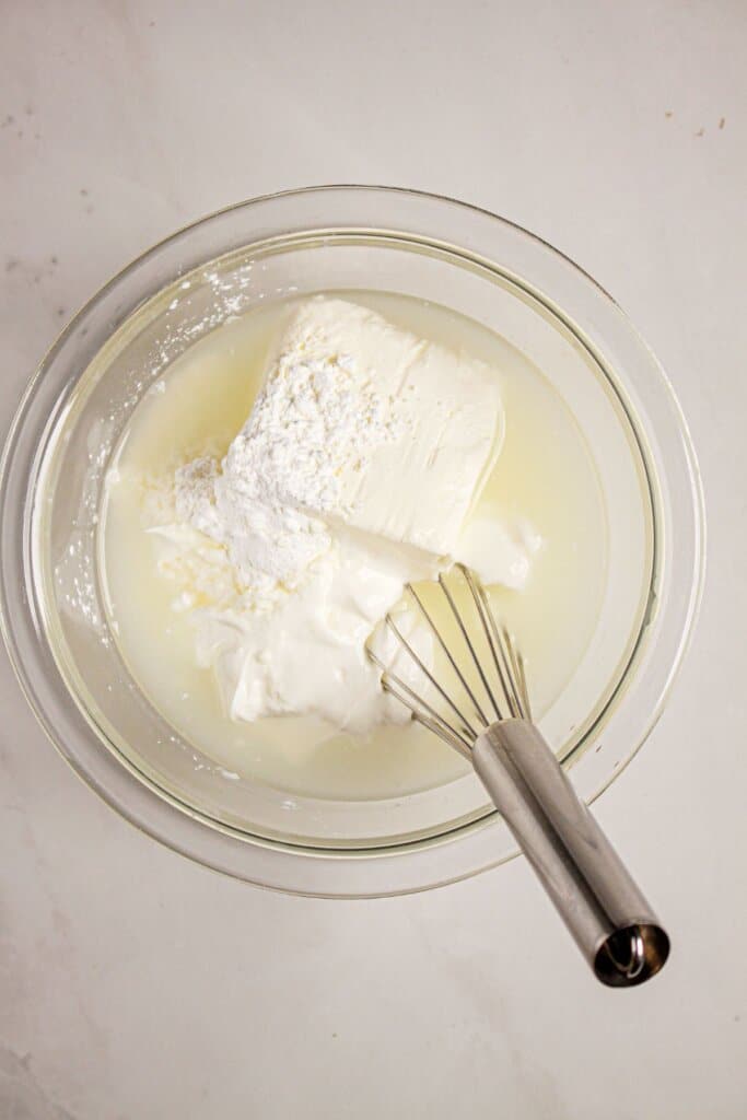 Sour cream and cream cheese being mixed in a glass bowl.