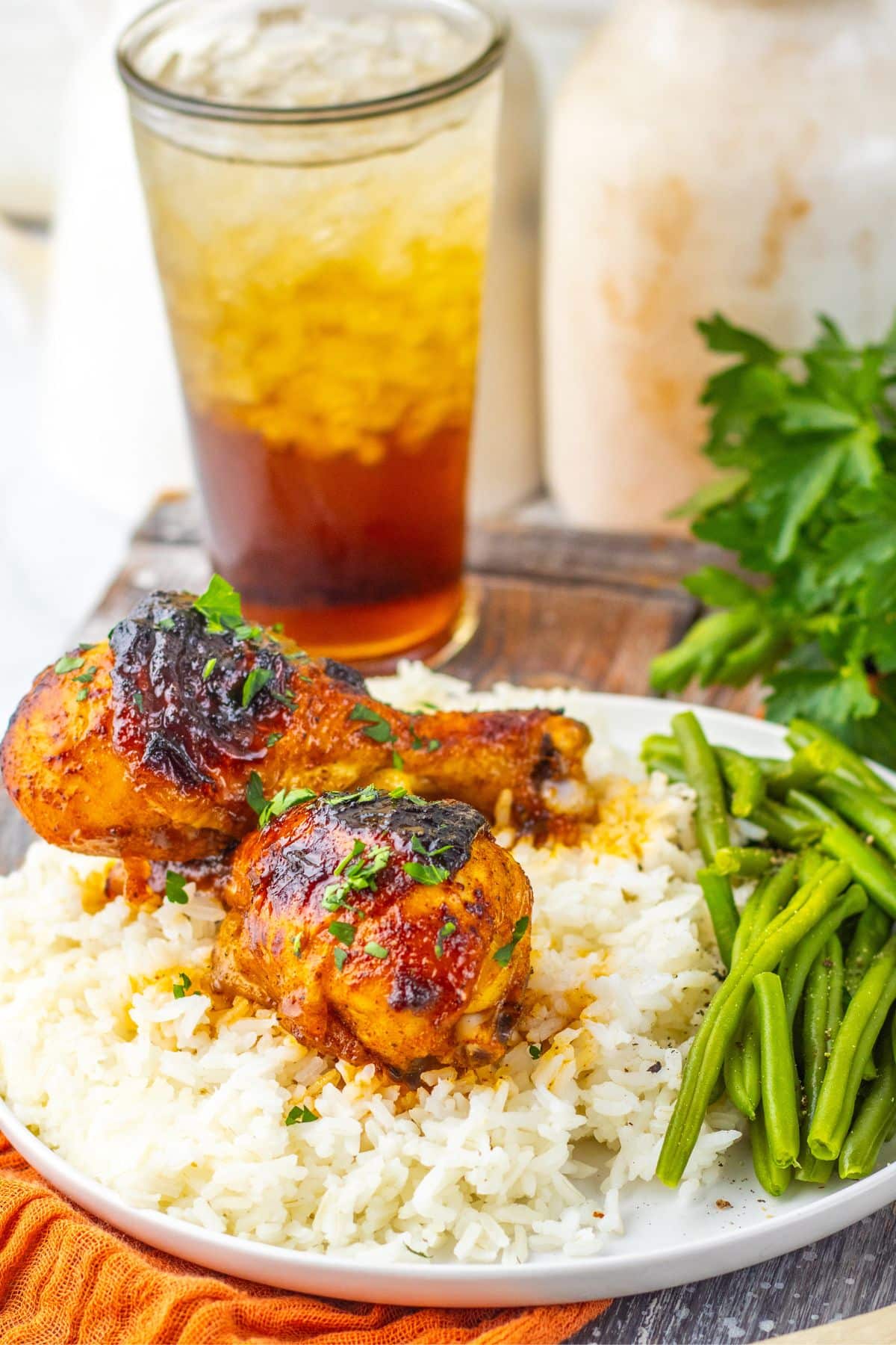 Two cajun chicken legs on a white plate with rice and green beans.