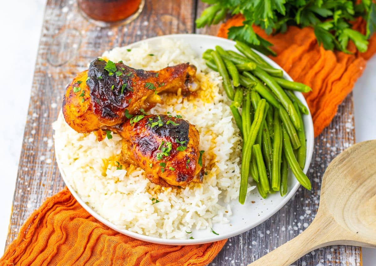 Two cajun chicken legs on a white plate with rice and green beans.