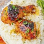 Two cajun chicken legs on a white plate with rice and green beans.