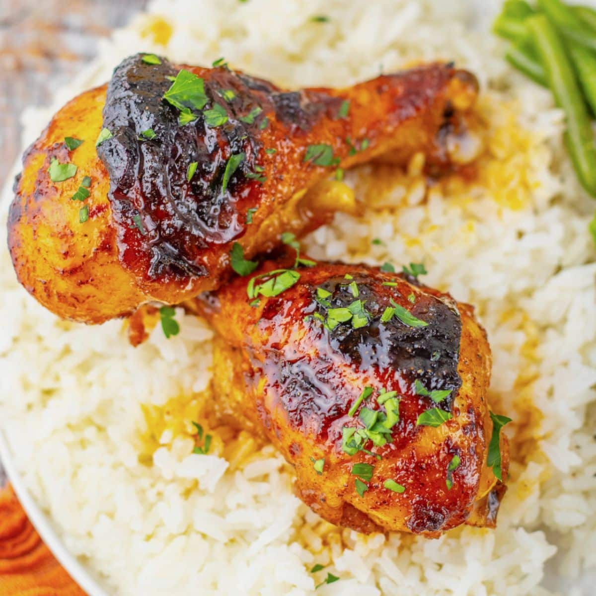 Two cajun chicken legs on a white plate with rice and green beans.