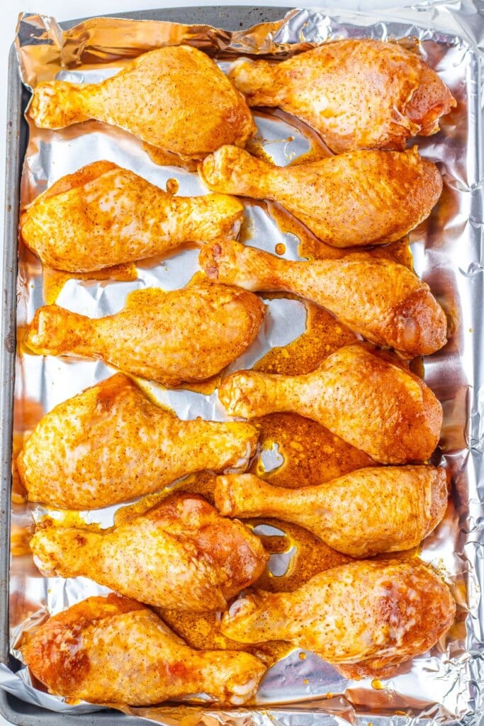 Seasoned drumsticks on a baking sheet ready for the oven.