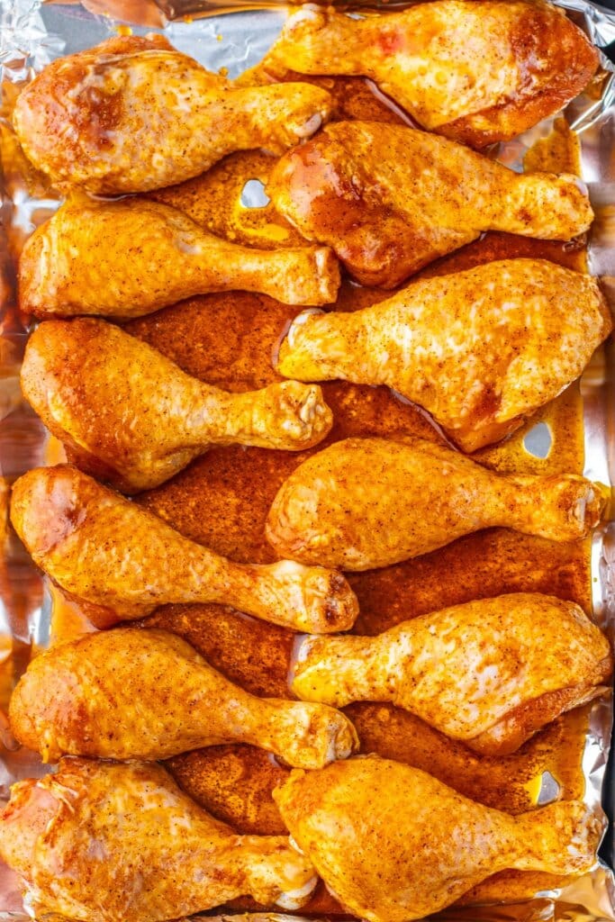 Drumsticks being seasonied on a baking dish.