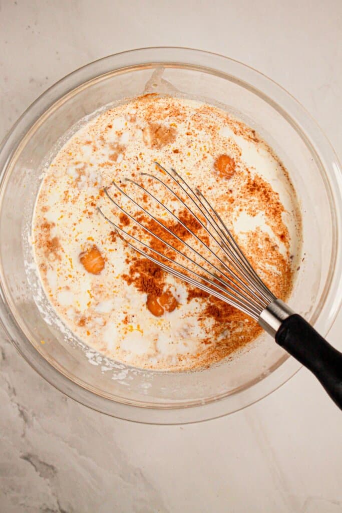 Custard being mixed in a glass mixing bowl.