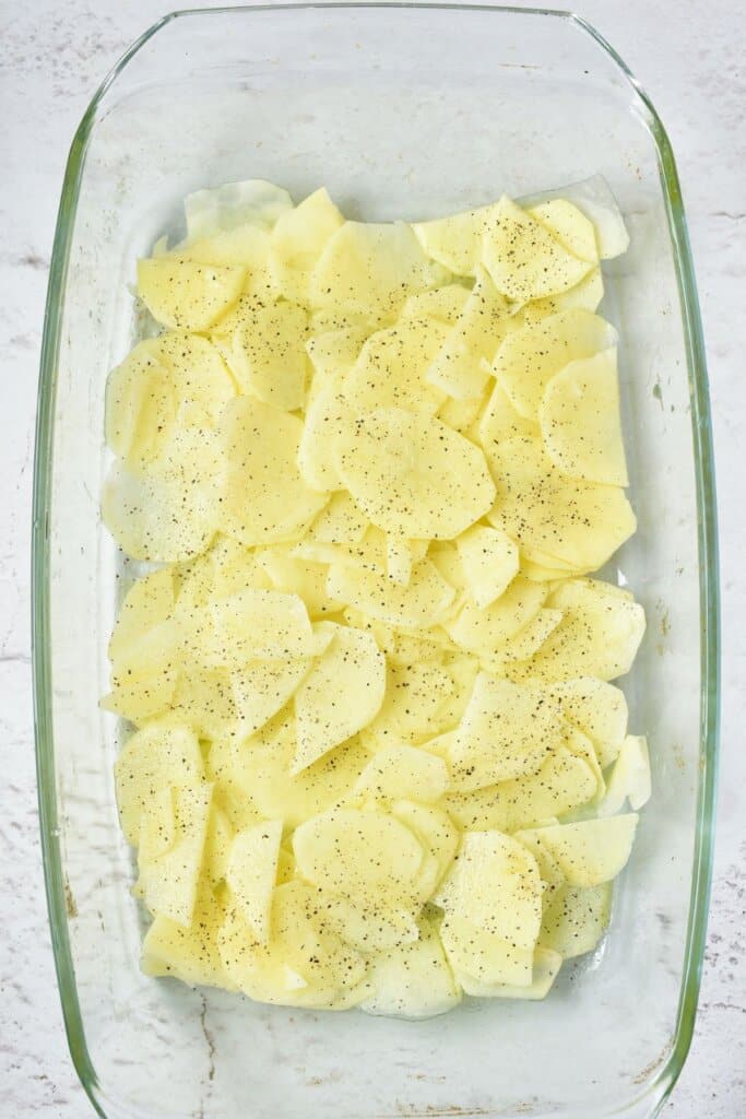 Sliced potatoes being layered in a glass baking dish.