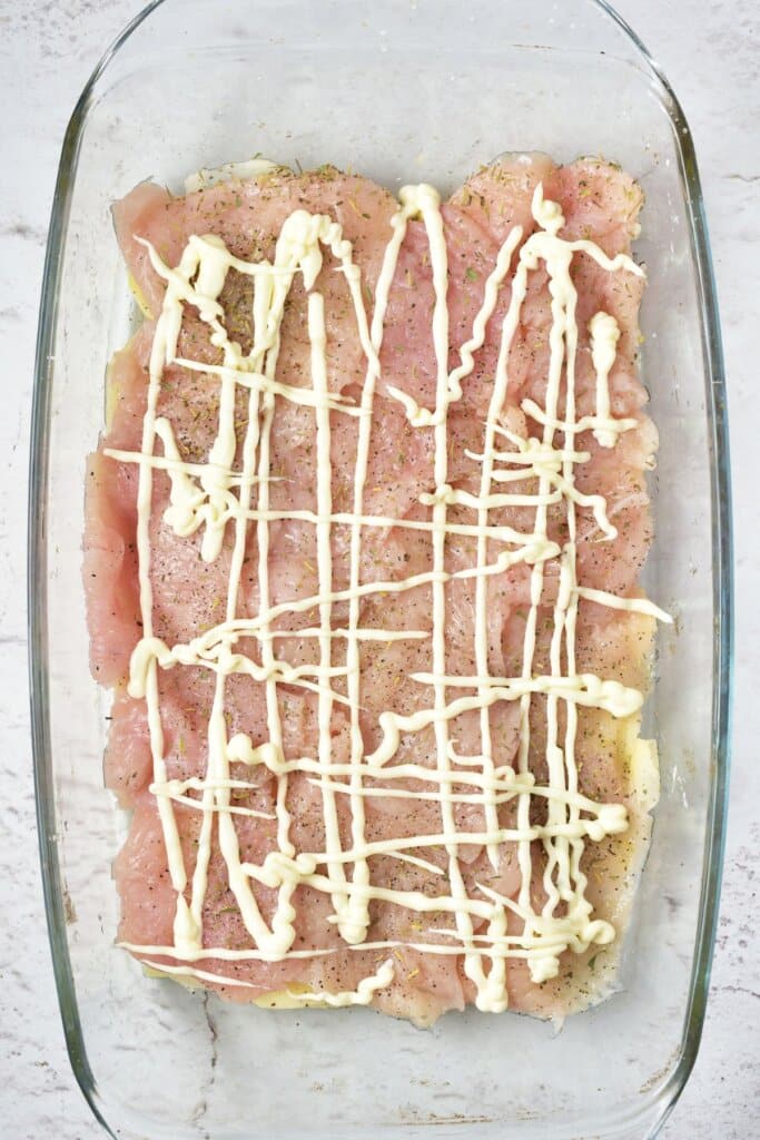 Mayo being spread on meat in a glass baking dish.