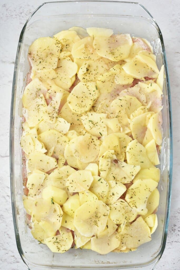 Potatoes being layered in glass baking dish.