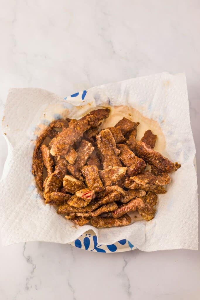 Beef strips draining on a paper towel.