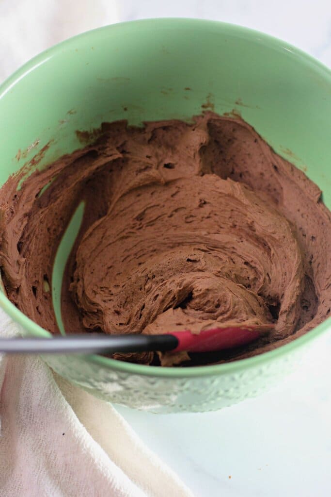 Frosting being mixed in a green mixing bowl.