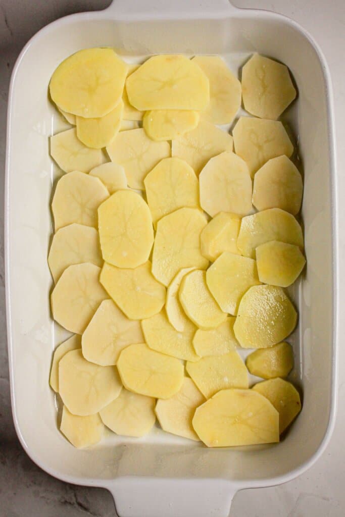 Raw potato slices in a white baking dish.