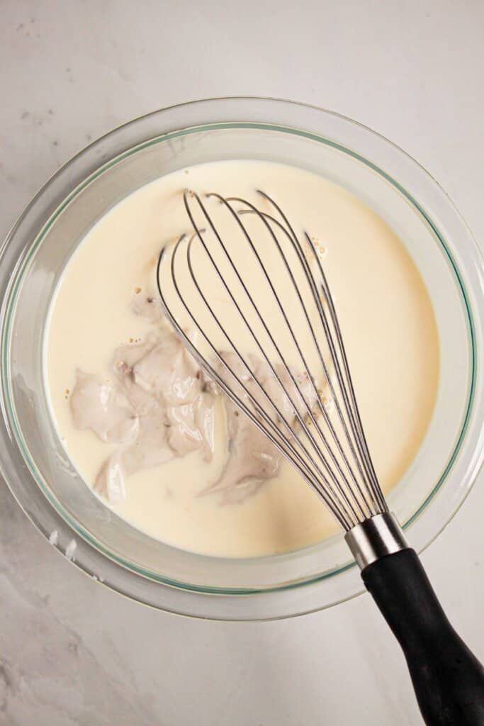 Mushroom soup and milk being mixed in a glass bowl.