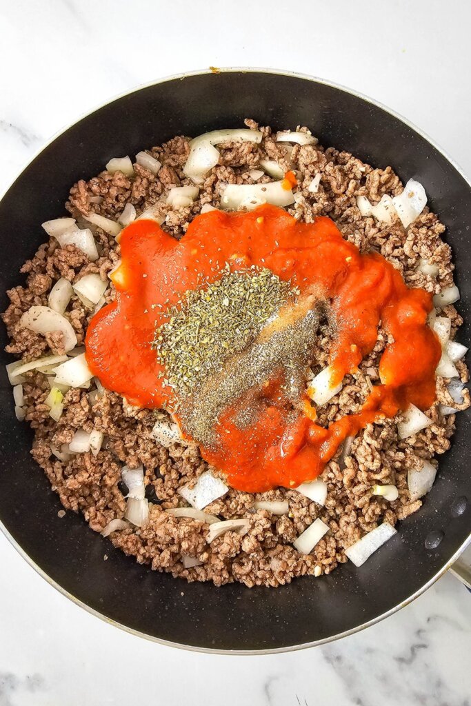 Cooked beef, onions, sauce, and seasoning in a skillet.