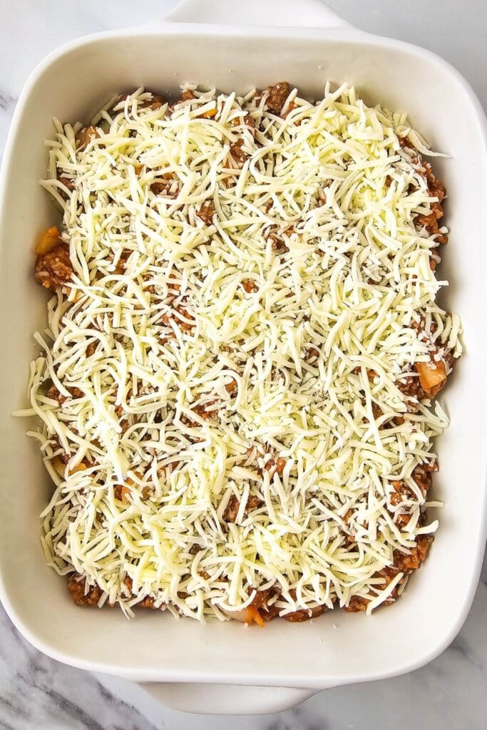 Shredded cheese on top of food in a white baking dish.