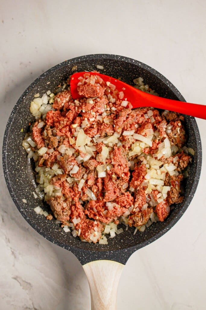 Beef and onions being cooked in a skillet.