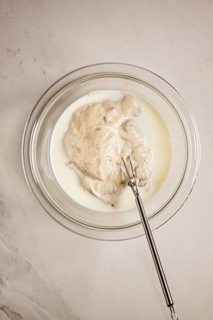 Cream of mushroom soup and milk being mixed in a glass bowl.