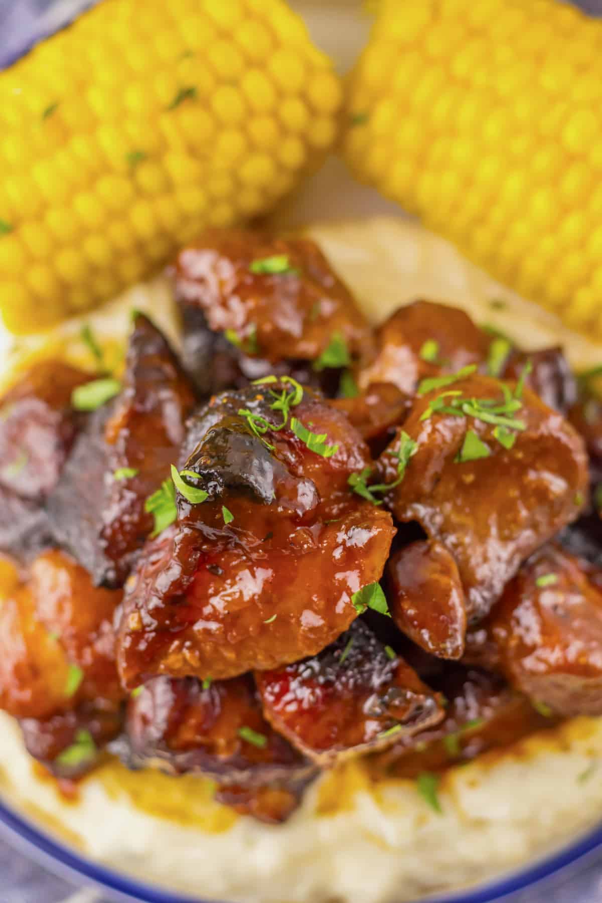Plate full of bbq riblets on top of mashed potatoes and corn on the cob.