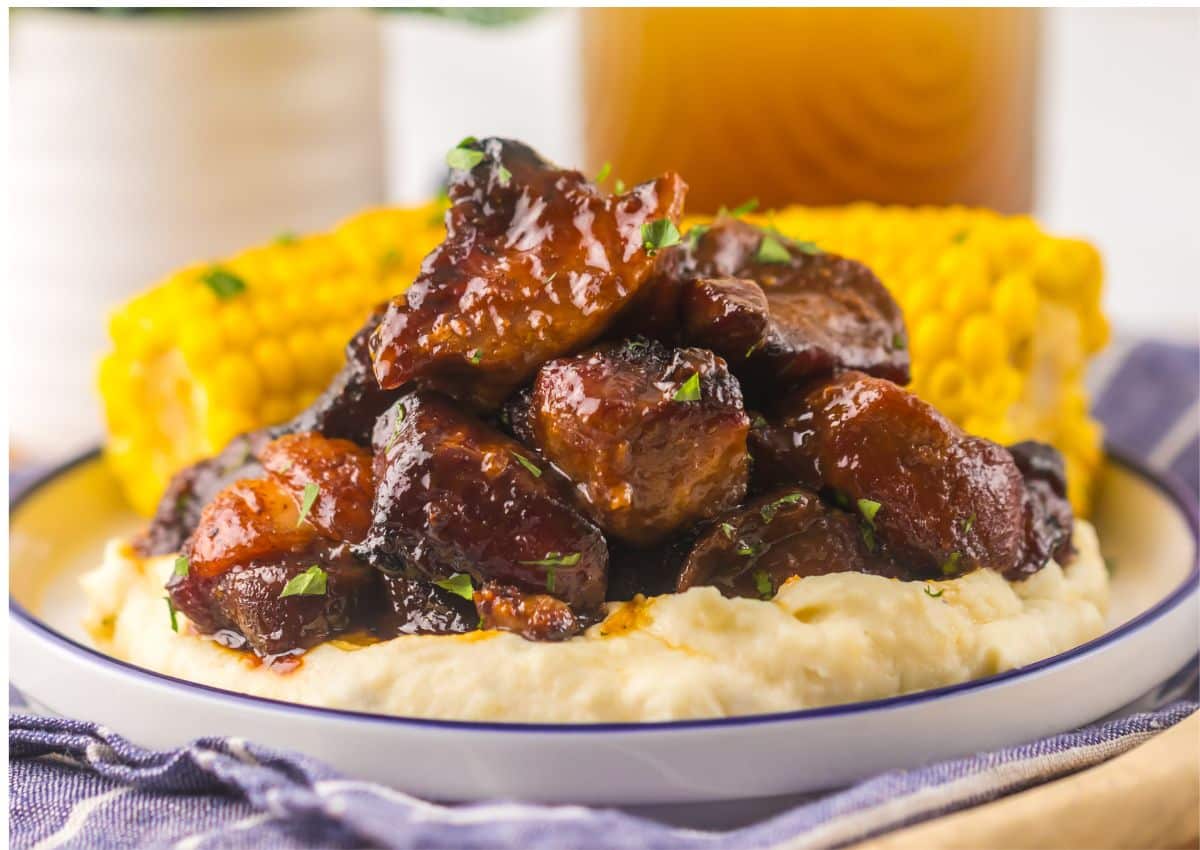 Plate full of bbq riblets on top of mashed potatoes and corn on the cob.