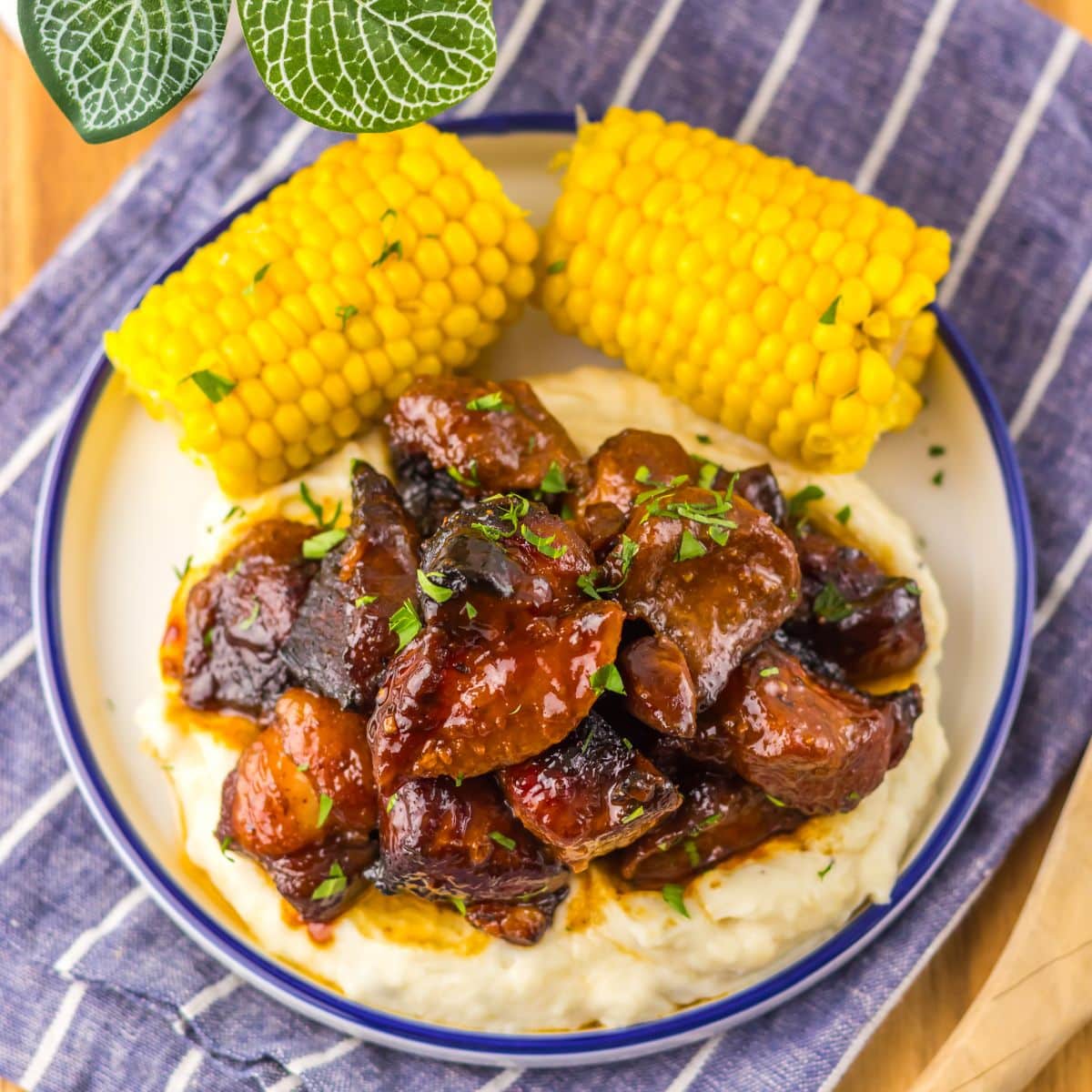 Plate full of bbq riblets on top of mashed potatoes and corn on the cob.