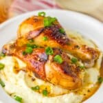 Two chicken drumsticks on top of a bed of mashed potatoes.