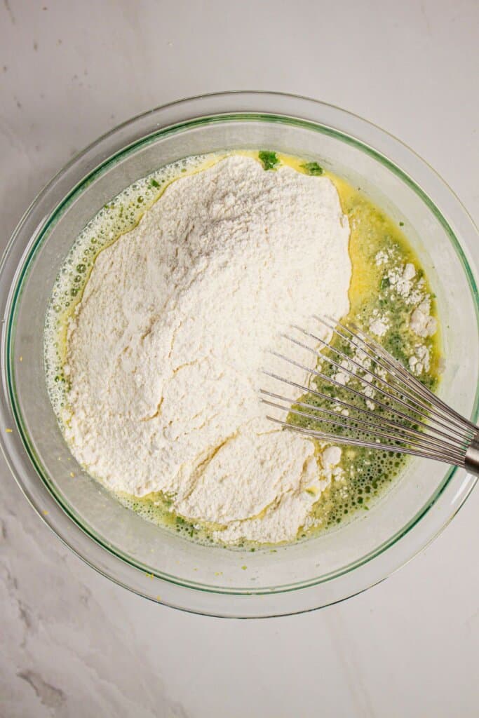 Dry ingredients being added to wet ingredients in a glass bowl.