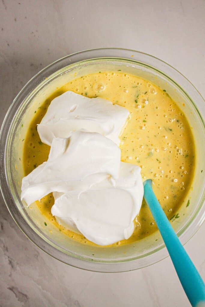 Egg whites being added to batter in a glass bowl.