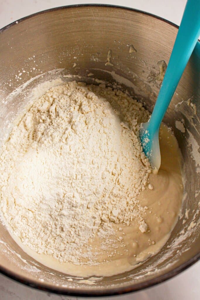 Flour being added to a stainless steel mixing bowl.