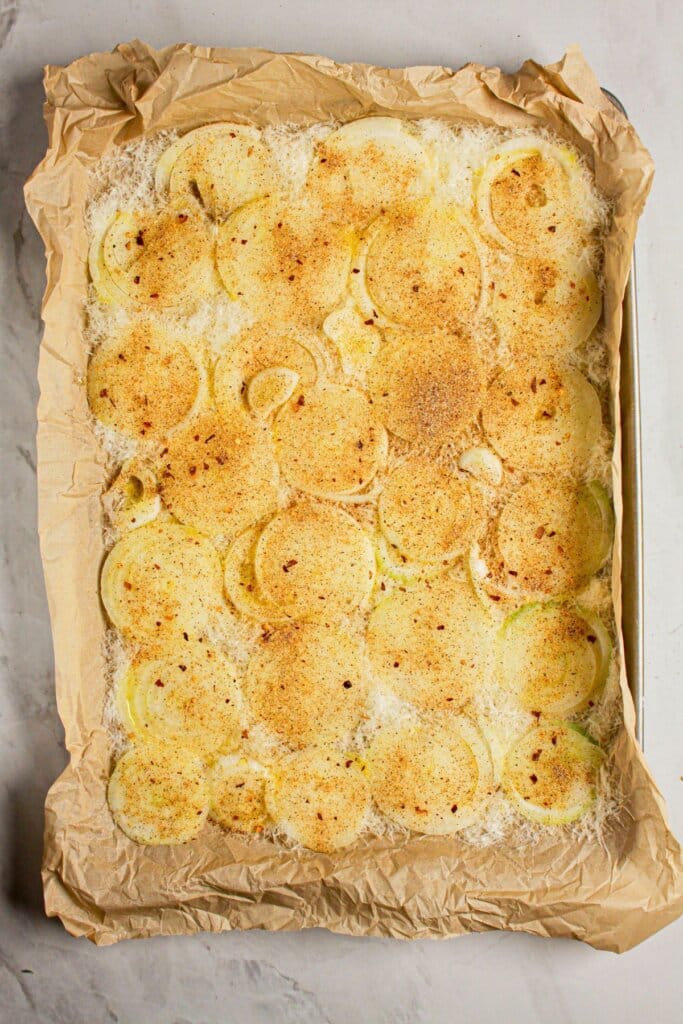 Vegetable and cheese being spread on a baking sheet.