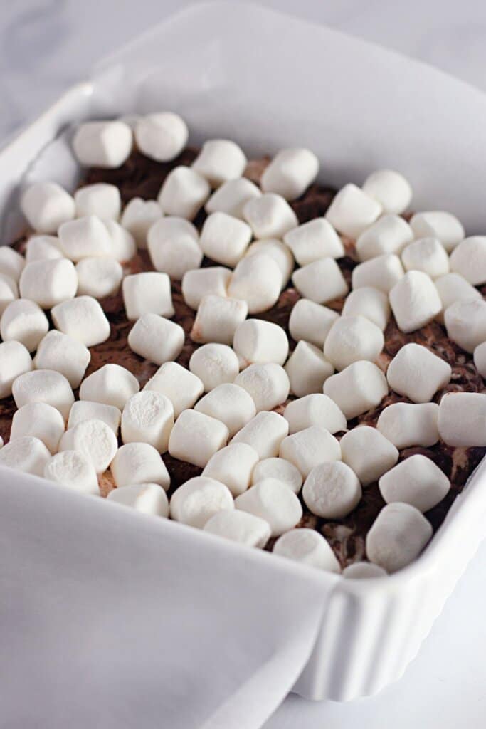 Marshmallows being sprinkled on top of candy in a baking dish.
