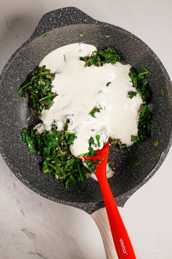 Cream being added to spinach in a skillet.