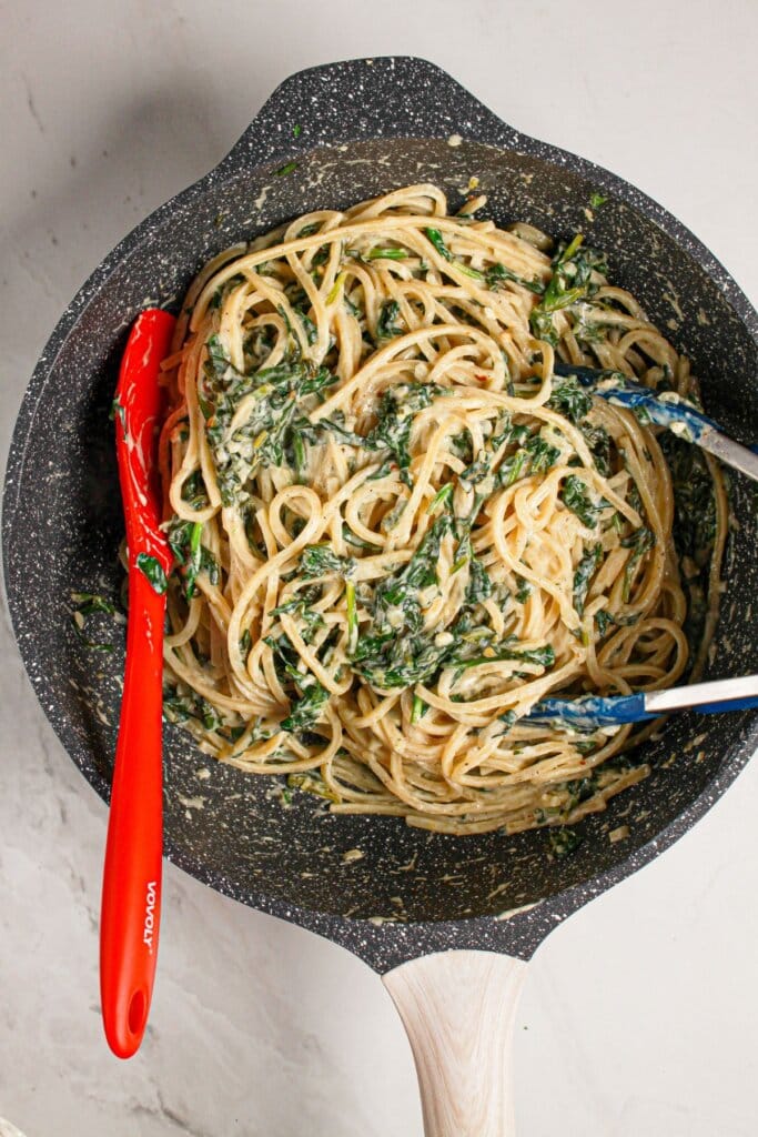Noodles being tossed in spinach tossed in a skillet.