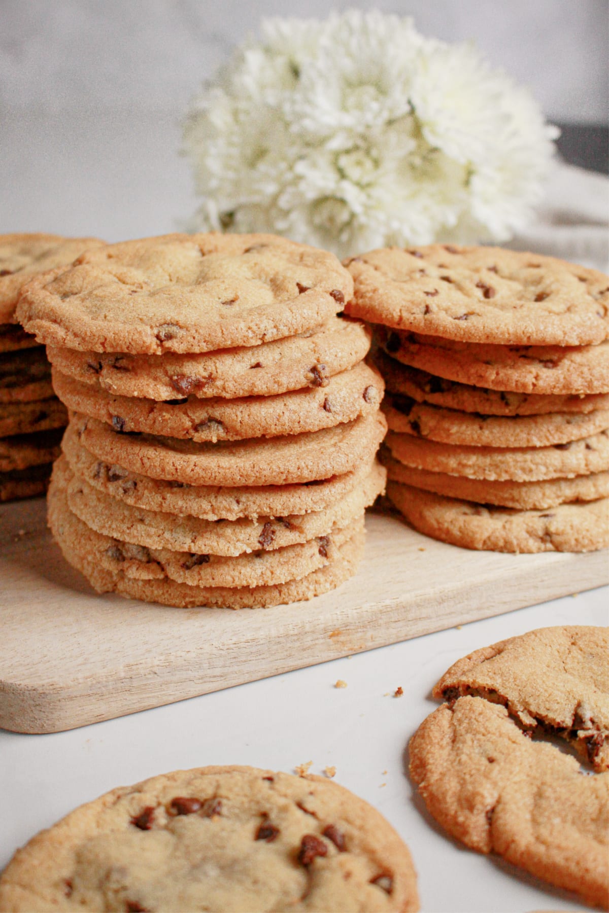 Stack of thin chocolate chip cookies on a wooden cutting board.