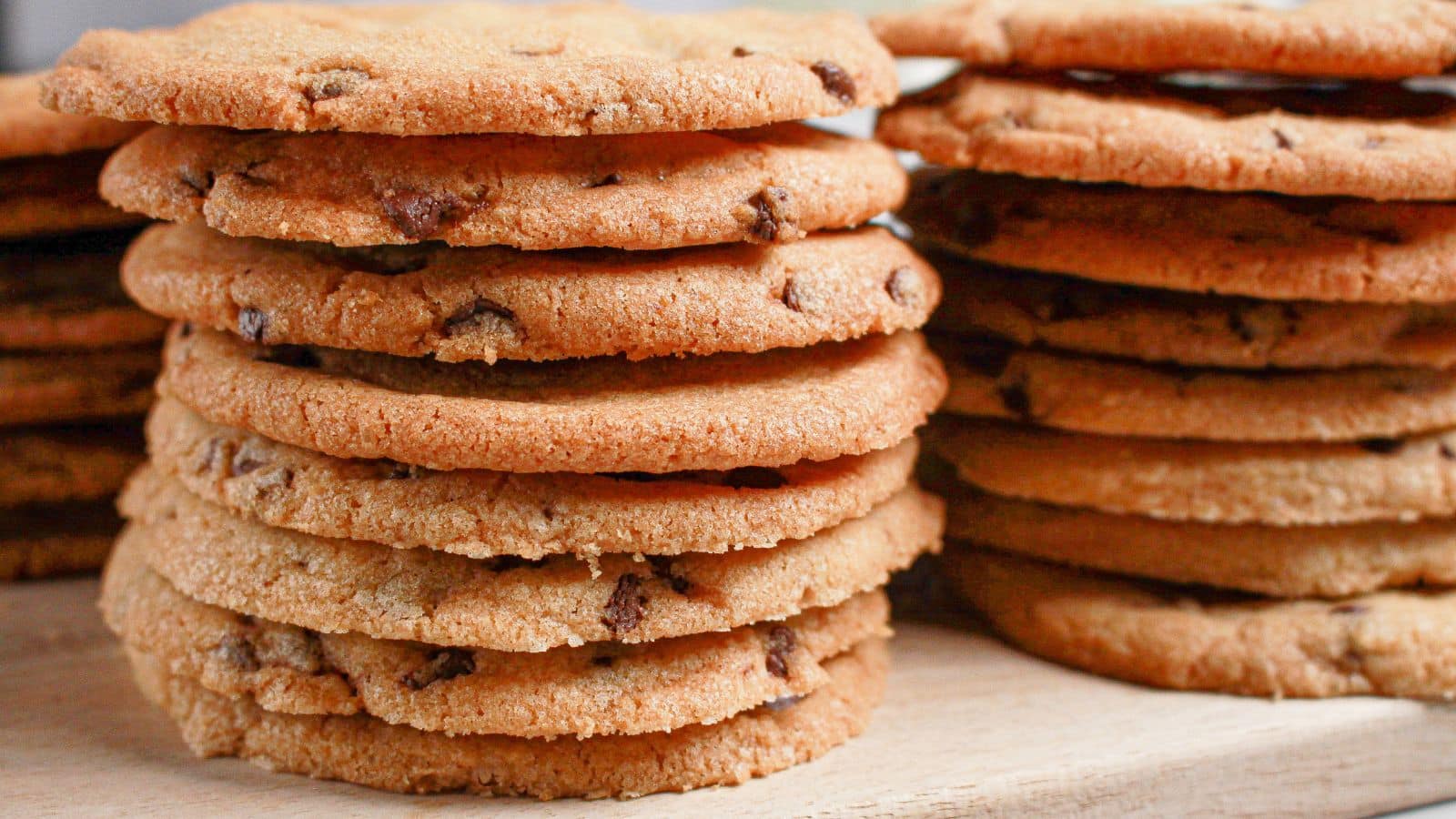 Stack of thin chocolate chip cookies on a wooden cutting board.