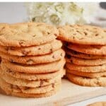 Stack of thin chocolate chip cookies on a wooden cutting board.