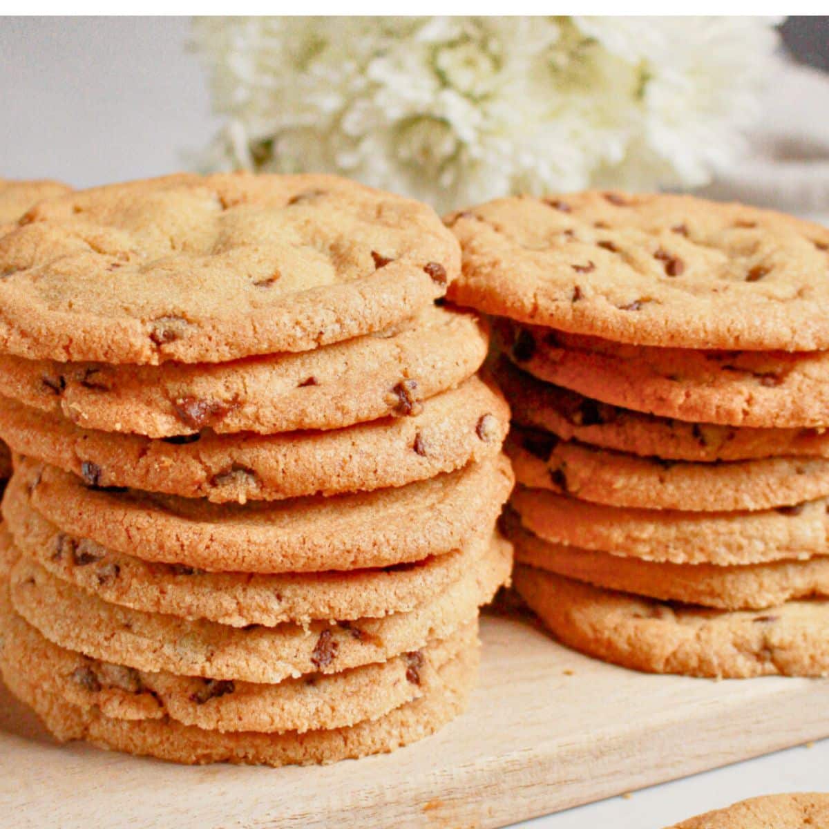 Stack of thin chocolate chip cookies on a wooden cutting board.