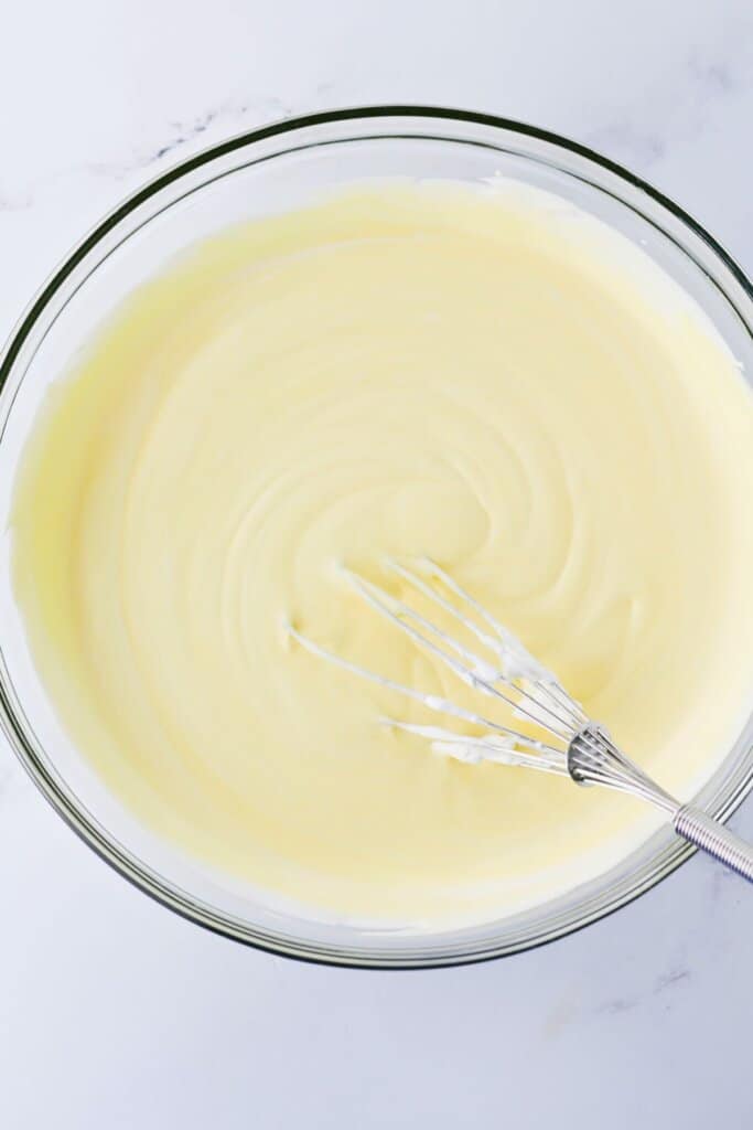 Creamy dessert ingredients being mixed in a large glass bowl.