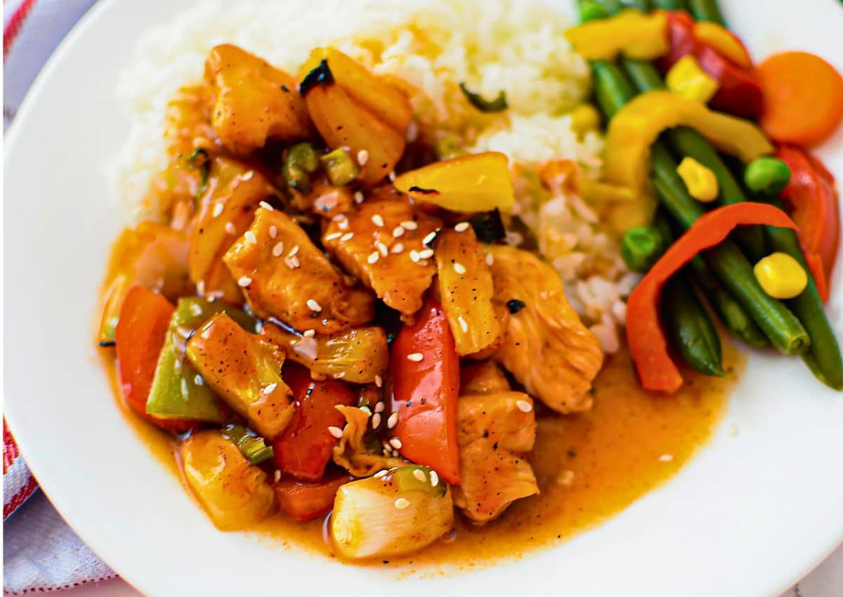 White plate full of rice, veggies, and bbq pineapple chicken.