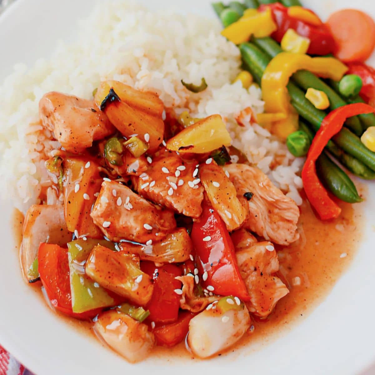 White plate full of rice, veggies, and bbq pineapple chicken.